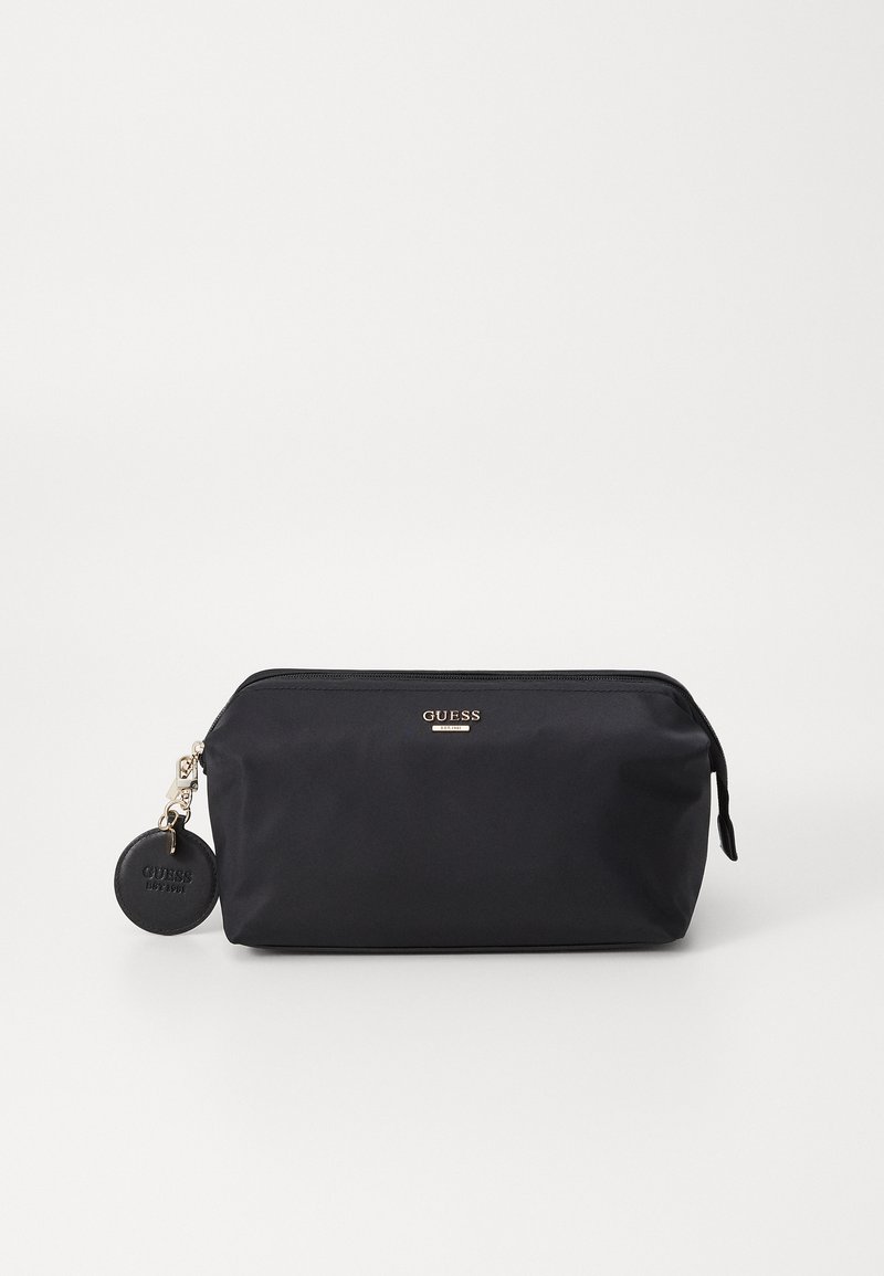 Pochette cosmétique en nylon noir avec une fermeture éclair, un logo doré, et une étiquette en cuir ronde attachée. Texture lisse et forme rectangulaire.