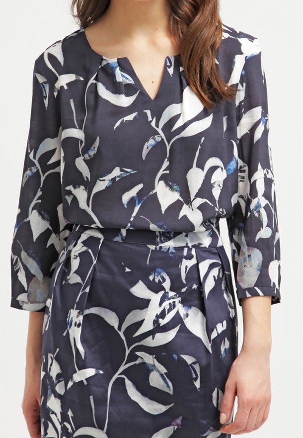 Blusa blu navy con motivo floreale bianco; presenta un scollo a V, maniche 3/4 e una vestibilità ampia. Realizzata in tessuto leggero con una leggera lucentezza.