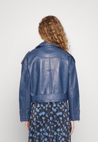 Blå läderjacka med en kort design, bred krage och axelkläppar. Slät textur, med detaljerad sömnad och justerbara manschetter.