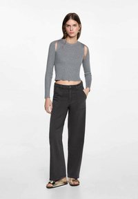 Maglione grigio corto con maniche lunghe e dettagli a taglio, abbinato a pantaloni neri a vita alta e gamba larga, insieme a sandali piatti. Design semplice.