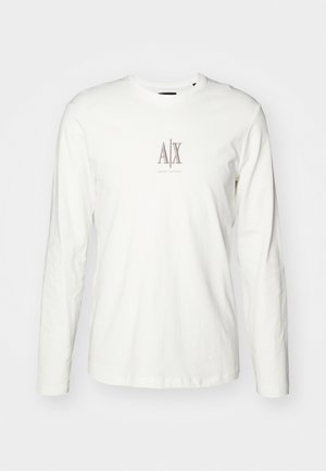 Pitkähihaisen valkoisen puuvillateepaidan etupuolella on pieni beigeklassinen logo, jossa lukee "AX" keskellä. T-paidassa on sileä pinta ja perinteinen pyöreä kaula-aukko.