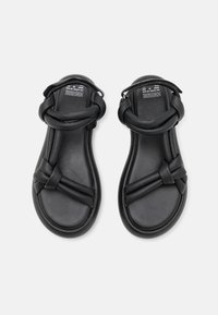 Black sandals with woven straps and a smooth, matte finish. Features a cushioned sole and adjustable ankle strap for comfort.