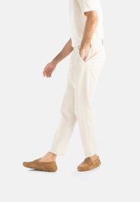 Pantaloni in lino beige con vestibilità affusolata, dotati di tasche laterali e una texture morbida. Indossati con mocassini in suede marroni.