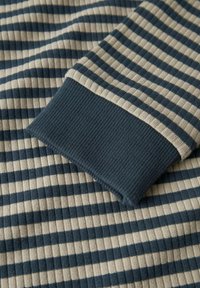 Nahaufnahme eines gestreiften Rippstrickstoffs mit beigen und dunkelblauen horizontalen Streifen sowie einem einfarbigen, dunkelblauen Rippbündchen.