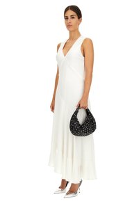 Abito bianco senza maniche con orlo a balze, abbinato a una borsa nera con pois bianchi. Tacchi a punta argentati completano l'outfit.