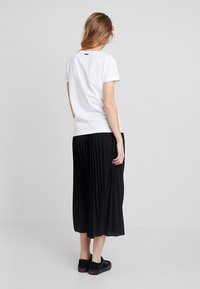 Bílý bavlněný tričko s krátkým rukávem v kombinaci s černou plisovanou midi sukní. Černé tenisky s červenými akcenty doplňují celý outfit.