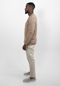 Een tan gebreide trui, beige chinos en lichtbeige suède instappers. De trui heeft een geribbelde zoom en manchetten, met een aansluitende silhouette.