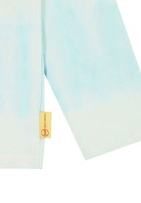 Camisa de manga larga azul claro con efecto degradado, hecha de tela suave. Presenta una pequeña etiqueta amarilla con texto rojo cerca del dobladillo.