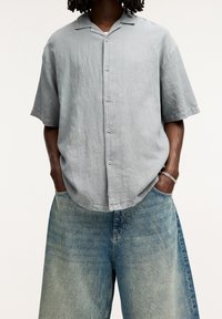 Camisa de manga corta gris claro, con botones en la parte delantera y un ligero cuello, combinada con unos vaqueros anchos de algodón con un acabado desgastado y un corte holgado.