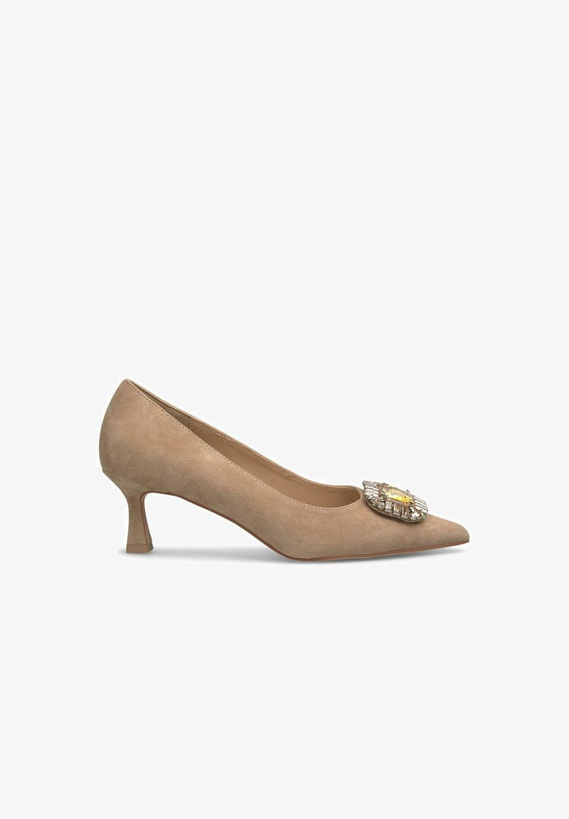 Beige suede hoge hak pump met een spitse neus en een middelhoge, uitlopende hak. Voorzien van een decoratieve sieradenversiering op de neus.