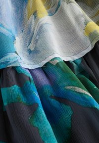 Close-up of layered sheer fabric with blue, green, yellow, and white abstract floral patterns and fine textured weave.