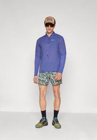 Lengvi ilgarankoviai violetinės spalvos sportiniai marškinėliai, šortai su gėlių raštu, juodos kojinės ir sportiniai bateliai su mėlynomis detalėmis.