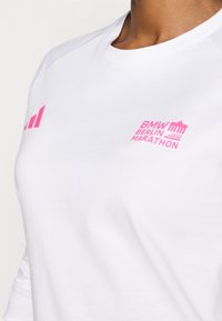 Hvid langærmet skjorte med pink "BMW Berlin Marathon" logo og design detaljer. Glat tekstur med rund halsudskæring og raglanærmer.