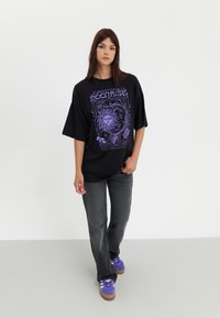 Black oversized t-shirt with purple graphic featuring a sun and floral designs; paired with dark gray jeans and purple sneakers.
