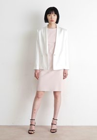 White blazer over a light pink dress, both fitted. Sandals with thin black straps. Smooth textures; minimalist design with no patterns.