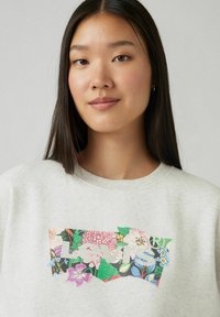 Sweatshirt gris clair avec un motif floral aux couleurs vives, comprenant du rose, du vert et du bleu. Col rond et texture douce.
