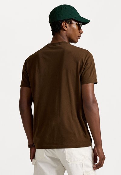 Camiseta de algodón marrón con cuello redondo, mangas cortas y una textura suave, combinada con una gorra verde y gafas de sol.
