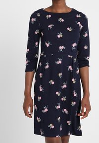 Marinblå klänning med trekvartslånga ärmar, som har blommig broderi i rosa och gult. A-linjeformad silhuett med rund nacke.