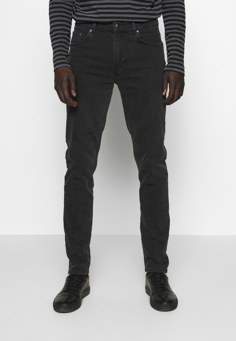 Jeans de mezclilla negra con un ajuste slim, que cuentan con cinco bolsillos, cierre de botón y detalles de costura a lo largo de las costuras. Combinados con zapatillas negras.