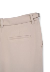 Pantalons beiges ajustés avec une texture lisse, poches latérales et arrière, et un détail de taille ceinturée avec une boucle en métal.