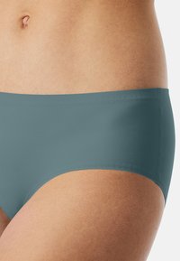 Teal hipster briefs made of smooth fabric, featuring a simple design with a midrise cut and elastic waistband.
