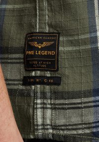 Geruite overhemd in groen en marineblauw, gemaakt van een gestructureerde stof. Bevat een zwart etiket met gouden lettertype met de tekst "PME Legend" en verzoeksinstructies.