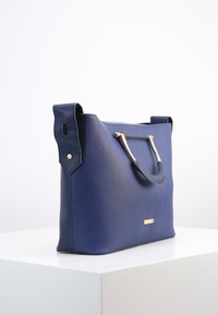 Modrá syntetická kabelka s texturovaným povrchem, strukturovaným designem, zlatými prvky a dvojitými rukojeťmi.