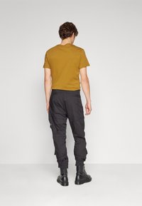 Černé cargo kalhoty s elastickými manžetami, doplněné hořčicovým tričkem s krátkým rukávem. Tento outfit doplňují černé kotníkové boty.