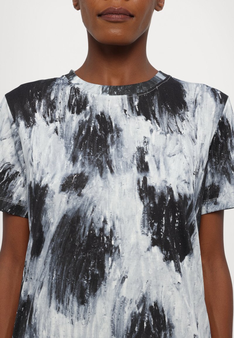 T-shirt à motif abstrait noir et blanc, à manches courtes, avec un col rond et un tissu légèrement texturé.