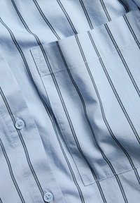 Hellblaues Hemd mit Knöpfen, das dünne schwarze vertikale Streifen, eine Brusttasche und eine glatte Baumwolltextur aufweist.
