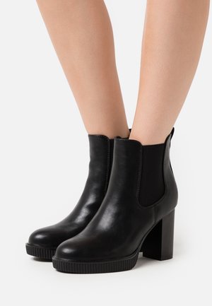 Botas de tobillo de cuero negro con paneles laterales elásticos, punta redondeada y un tacón ancho, con una suela de goma texturizada.