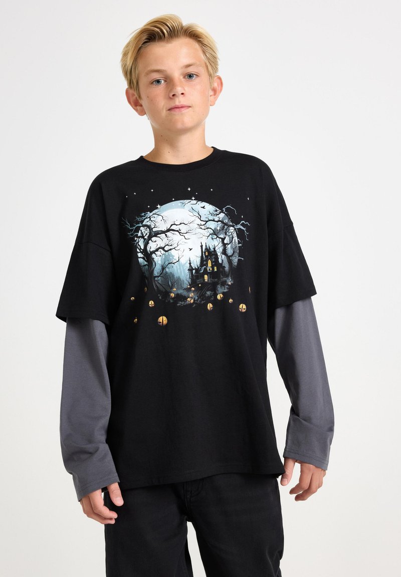 Schwarzes Grafik-T-Shirt mit einer mondbeschienenen Szene, die Bäume und ein Schloss zeigt, mit grauen Langärmeln, die an den Bündchen sichtbar sind. Normale Passform.