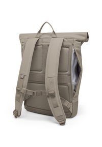 Beigen värinen yläkääntöreppu nähtynä takaa, jossa on pehmustetut verkkohihnat, säädettävä rintalukko ja sivussa vetoketjuavaus.