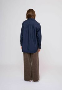 Tengerészkék bő fazonú ing galléros nyakkal, hosszú ujjakkal és elasztikus fodros szegéllyel. Széles kordbársony nadrággal párosítva.