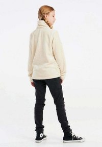 Pullover in pile beige con colletto alto, abbinato a pantaloni neri slim-fit e sneakers nere alta con logo a stella bianca.