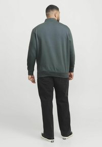 Hanorac verde închis cu guler înalt, cu manșete și tiv cu nervuri, asociat cu pantaloni negri drepti și ghete negre. Design minimalist.