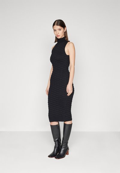Rochie tricotată neagră cu guler înalt, având un model texturat în romburi. Asortată cu cizme negre din piele până la genunchi, cu vârf pătrat.
