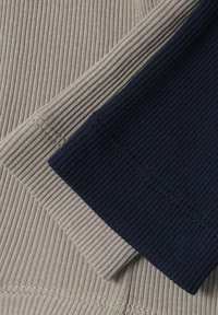 Tissu en maille côtelée beige et bleu marine foncé plié avec coutures visibles et détails de texture.