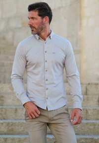 Helles graues Hemd mit Knöpfen, einer strukturierten Musterung und einem dezenten Logo, kombiniert mit beigen Hosen. Verfügt über lange Ärmel und einen klassischen Kragen.