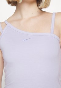 Kvinna som bär en ljuslila asymmetrisk linne med dubbla axelband och en liten Nike-logga på bröstet.