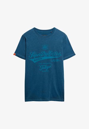 T-shirt in cotone blu con collo rotondo. Presenta un logo stampato in serigrafia di un blu chiaro e un'accento arancione sulla manica. Materiale leggero.