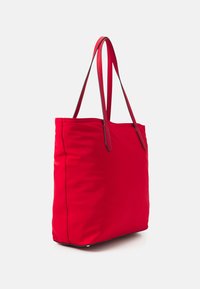 Czerwona torba na ramię wykonana z miękkiego materiału z dwoma cienkimi uchwytami. Charakteryzuje się prostym, nieozdobionym wzornictwem oraz prostokątnym kształtem.