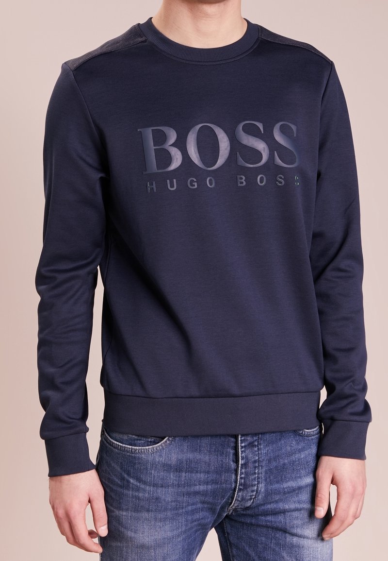 Námořnická modrá mikina vyrobená z bavlněné směsi, která má na přední straně vyvýšené logo "BOSS HUGO BOSS", žebrované manžety a pas.