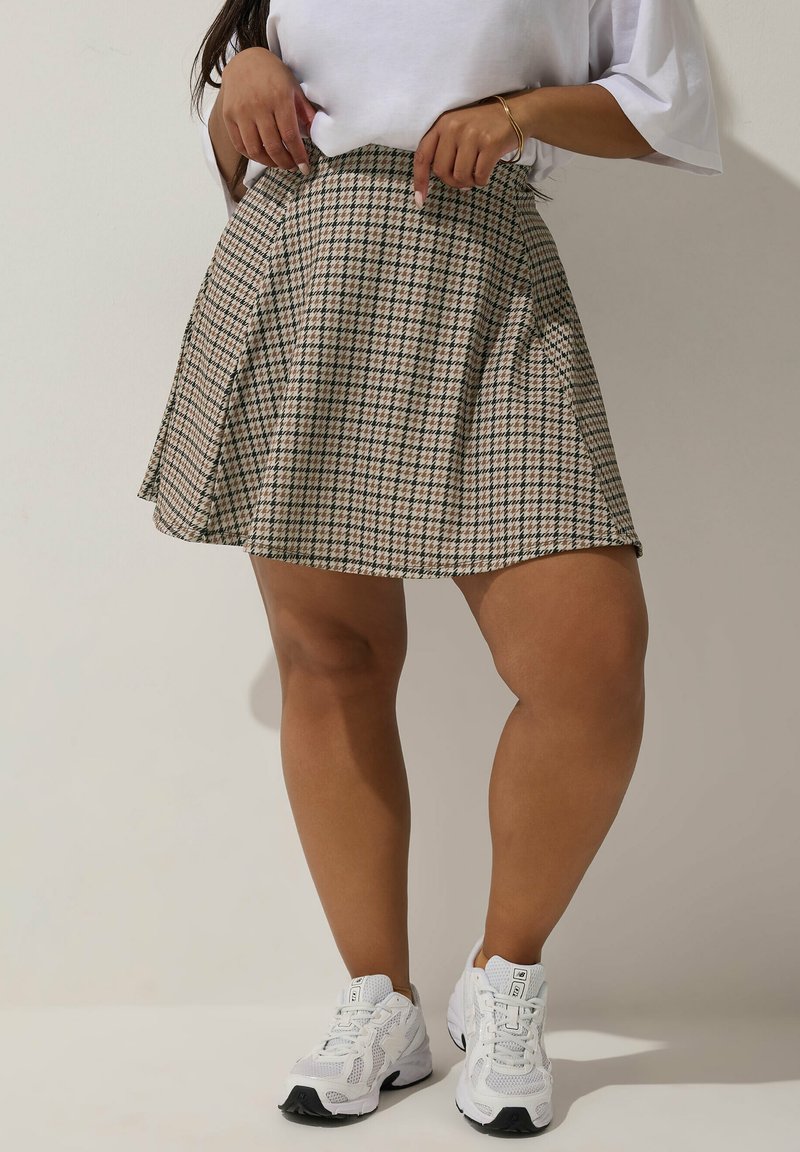 Beige geruite rok met een uitlopende ontwerp, voorzien van een hoge taille en plooien. Gecombineerd met witte sportschoenen.