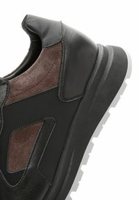 Baskets en cuir noir avec des accents en daim marron, dotées d'une semelle blanche épaisse. Le design comprend des découpes et des détails de couture.