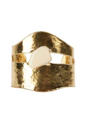 Ancho brazalete de oro martelé con una piedra blanca irregular centrada en un corte horizontal abierto.