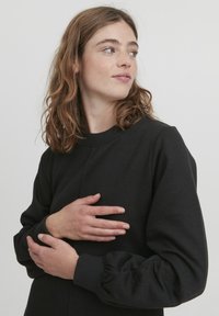 Felpa nera in cotone, con scollatura rotonda e maniche a sbuffo. Tessuto morbido con polsini a coste e design minimale.