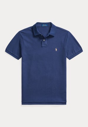 Tamsiai mėlyna polo marškinėlių, pagamintų iš tekstūrinio audinio. Yra apykaklė, trumpomis rankovėmis ir mažas siuvinėtas logotipas kairėje krūtinės pusėje.