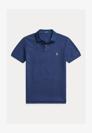 Tamsiai mėlyna polo marškinėlių, pagamintų iš tekstūrinio audinio. Yra apykaklė, trumpomis rankovėmis ir mažas siuvinėtas logotipas kairėje krūtinės pusėje.