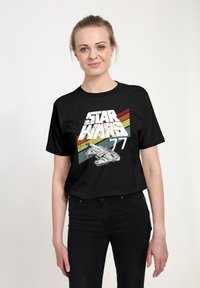 Černé tričko s nápisem "STAR WARS 77" a grafikou vesmírné lodě spolu s barevnými šikmými pruhy v červené, oranžové a modré barvě.